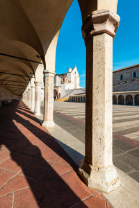 Blick durch Säulen auf die Basilika des Hl. Franziskus von Assisi in der Morgensonne, Umbrien, Italien