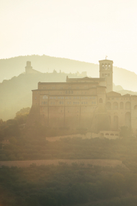 Die Festung Rocca Maggiore, die Basilika und das Kloster des Hl. Franziskus und die Altstadt von Assisi im Gegenlicht der Morgensonne, Umbrien, Italien