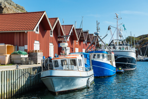 Gebäude mit typischen roten Holzfassaden und Fischerboote im Hafen von Skärhamn in den Schären der Insel Tjörn im Sommer, Bohuslän, Schweden