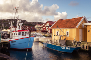 Fischerboote an der hölzernen Hafenmole vor einer gelber Fischerhütte im Hafen von Björholmen in den Schären der Insel Tjörn, Bohuslän, Schweden
