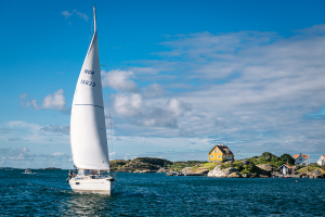 Yacht mit gesetzen Schratsegel durchfährt bei Morgensonne den Sund zwischen den Inseln Tjörn und Härön bei Kyrkesund in den Schären der schwedischen Westküste