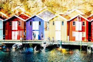 Bootsschuppen und Speicherhäuser mit bunten Holzfassaden zwischen Granitfelsen an der Hafenpromenade von Smögen in den Schären der schwedischen Westküste bei Sonnenschein
