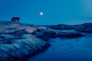 Der Mond über einer Holzhütte auf Felsen am Ufer des Skagerraks im Naturreservat Tjurpannan in den Schären der schwedischen Westküste