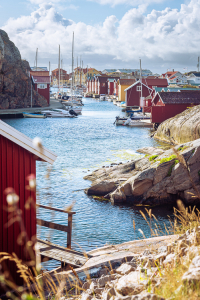 Bootsschuppen und Speicherhäuser mit roten Holzfassaden und Granitfelsen im Hafen von Smögen in den Schären der schwedischen Westküste bei Sonnenschein