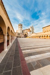 Säulengänge umgeben den unteren Platz vor der Basilika des Hl. Franziskus von Assisi im Abendlicht, Umbrien, Italien